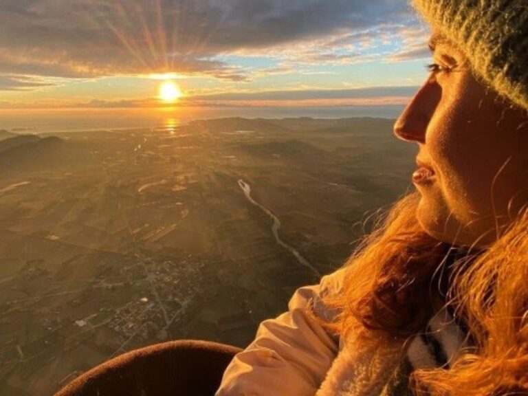 A woman gazes at the sky while traveling in a hot air balloon over Ampurdà. The sun shines brightly and the altitude is evident.